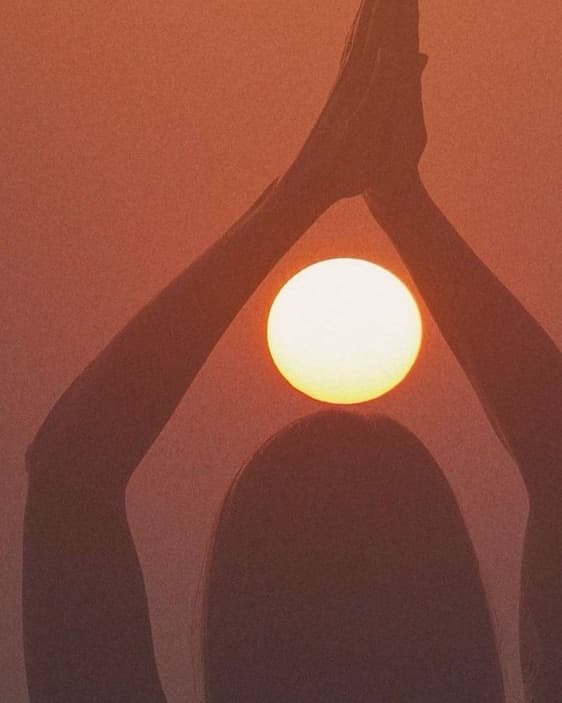 Hands joined above the head against the setting sun