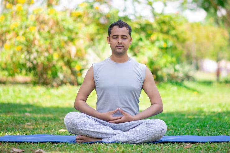 Host meditating cross-legged on a mat in a garden